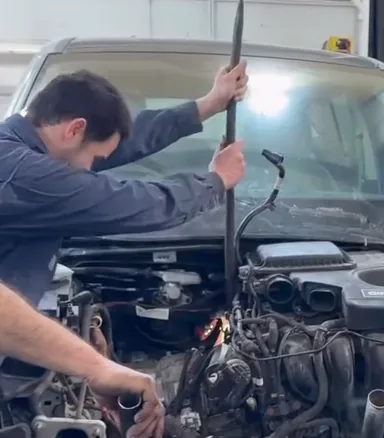 A mechanic leaning into an engine bay with the engine pulled out, in the RM shop