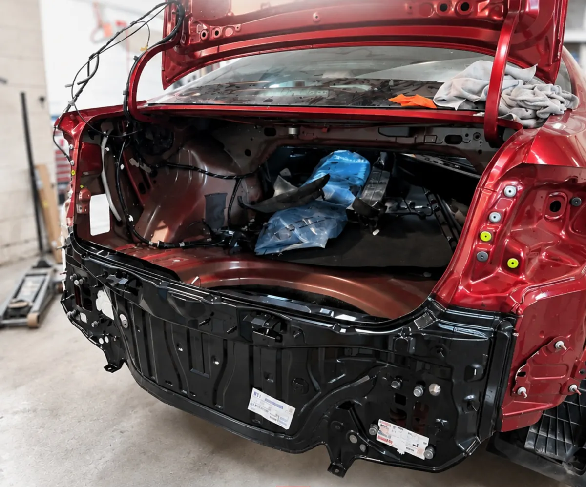 The same red sedan with a new rear body panel installed, still disassembled